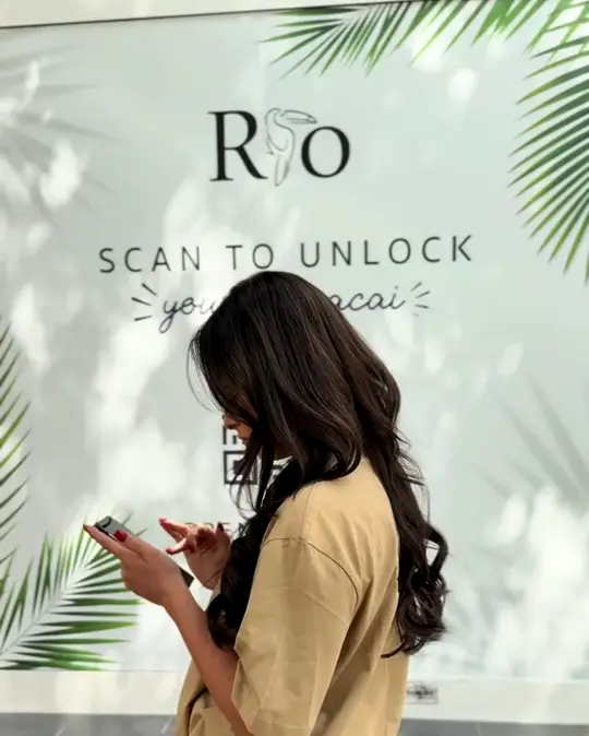 Plakat „Scan to unlock your free açaí“ am Schaufenster, davor eine Frau mit Handy