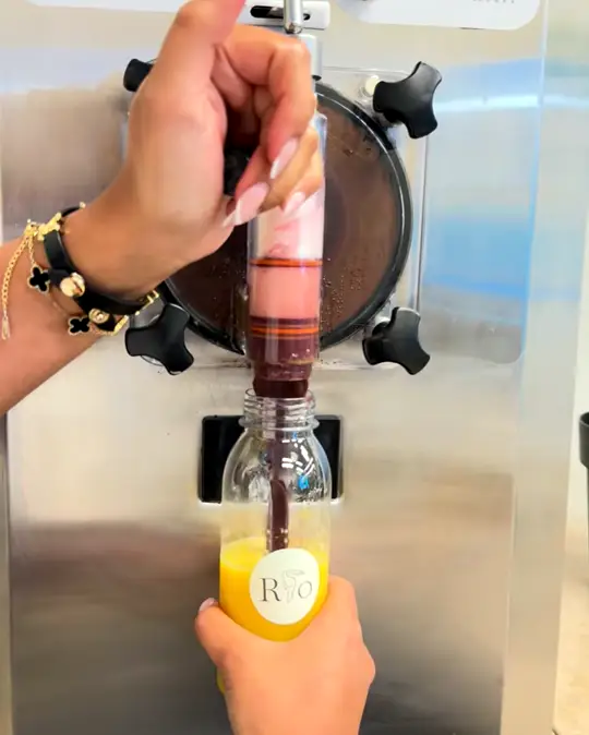 Flasche mit Orangensaft wird an der Açaí-Maschine mit Açaí gefüllt
