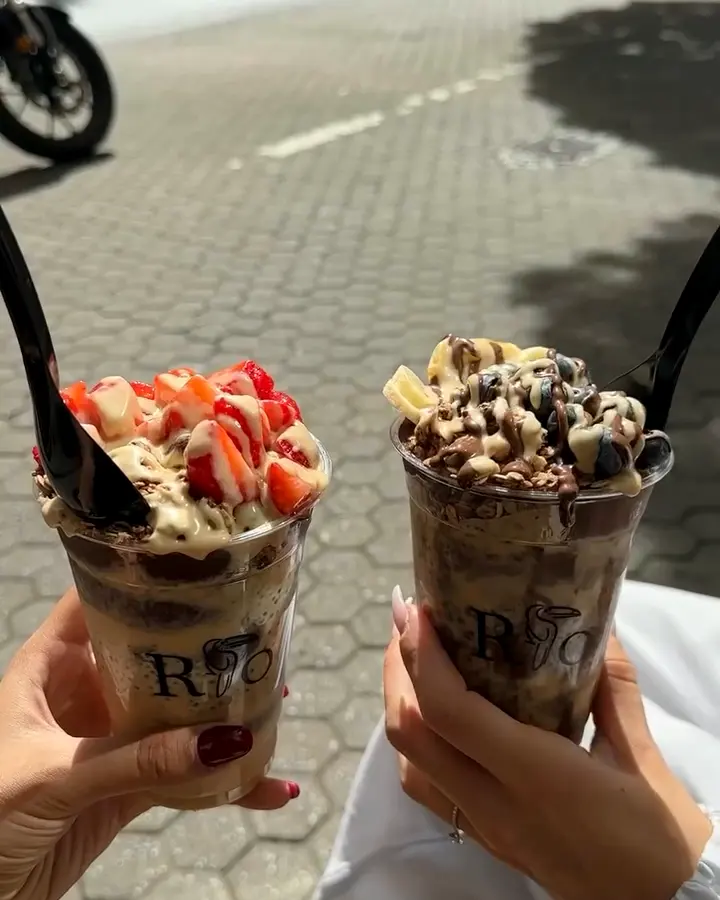 Zwei RIO-Becher mit Erdbeeren und Schoko-Topping, draußen auf der Straße
